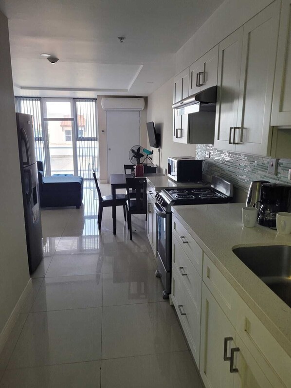 A modern kitchen with white cabinetry, a stainless steel stove, and a microwave. There is a dining area with a table and chairs, and a refrigerator is visible in the corner.