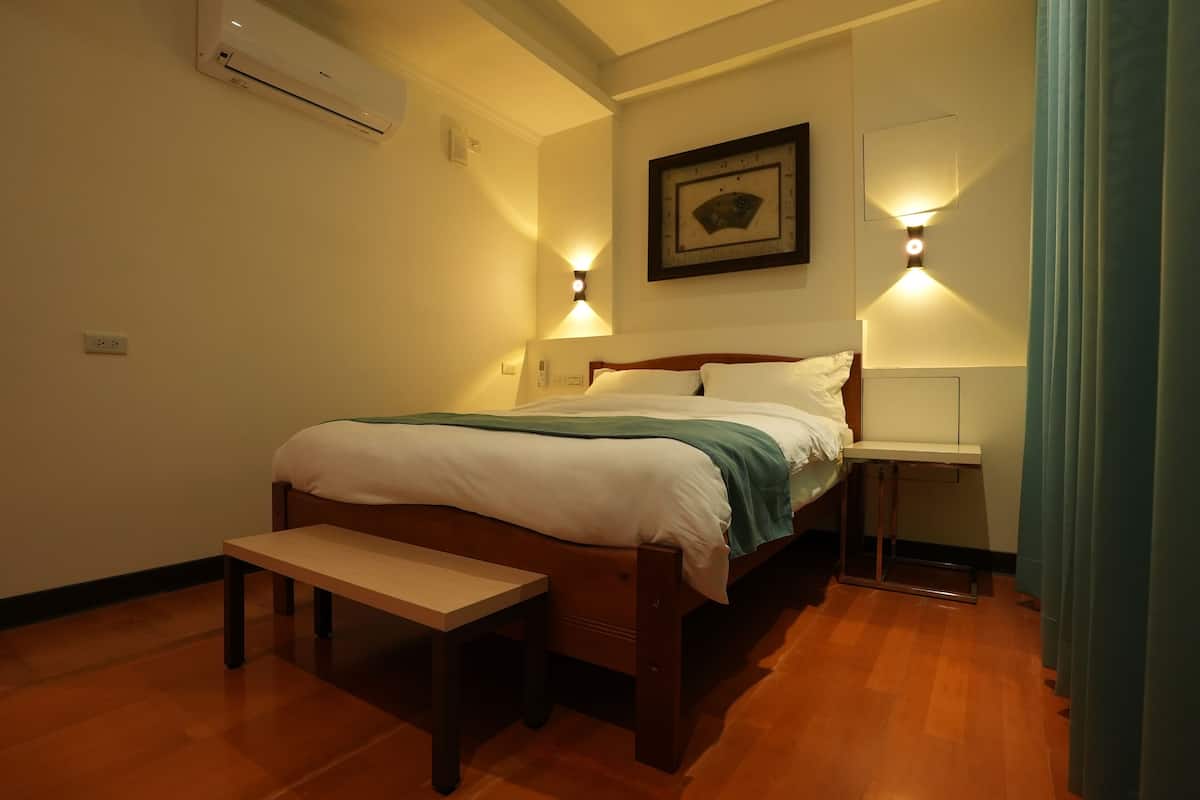 Quarto com cama de madeira, mesas de cabeceira, um banco, ar condicionado e luminárias fixadas na parede.
