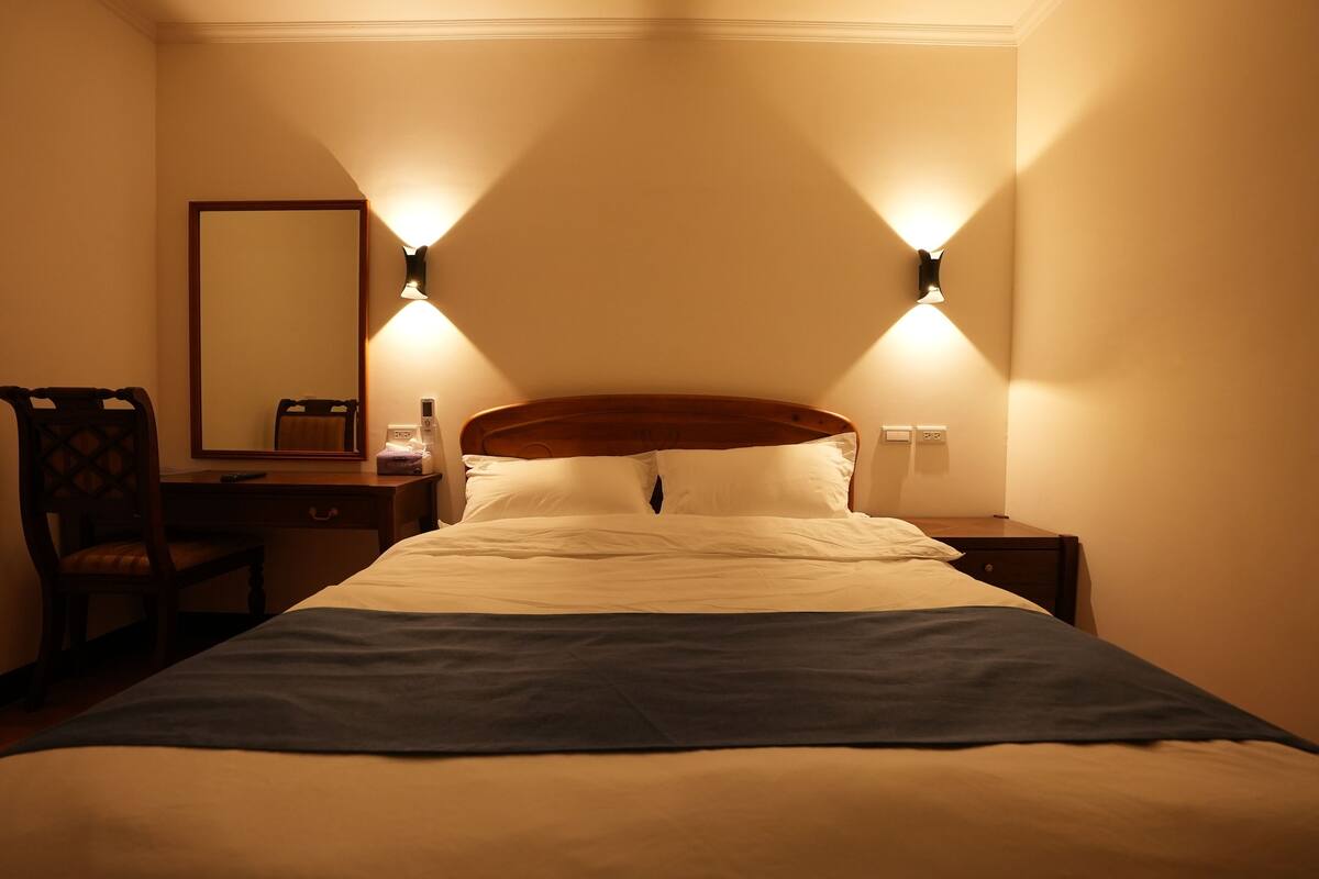 Quarto de hotel com uma cama, duas mesas de cabeceira, uma luminária e um espelho.
