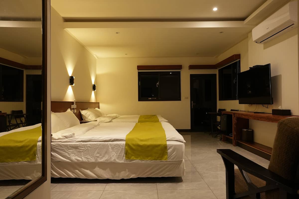 Quarto de hotel com duas camas, televisão, escrivaninha e espelho.