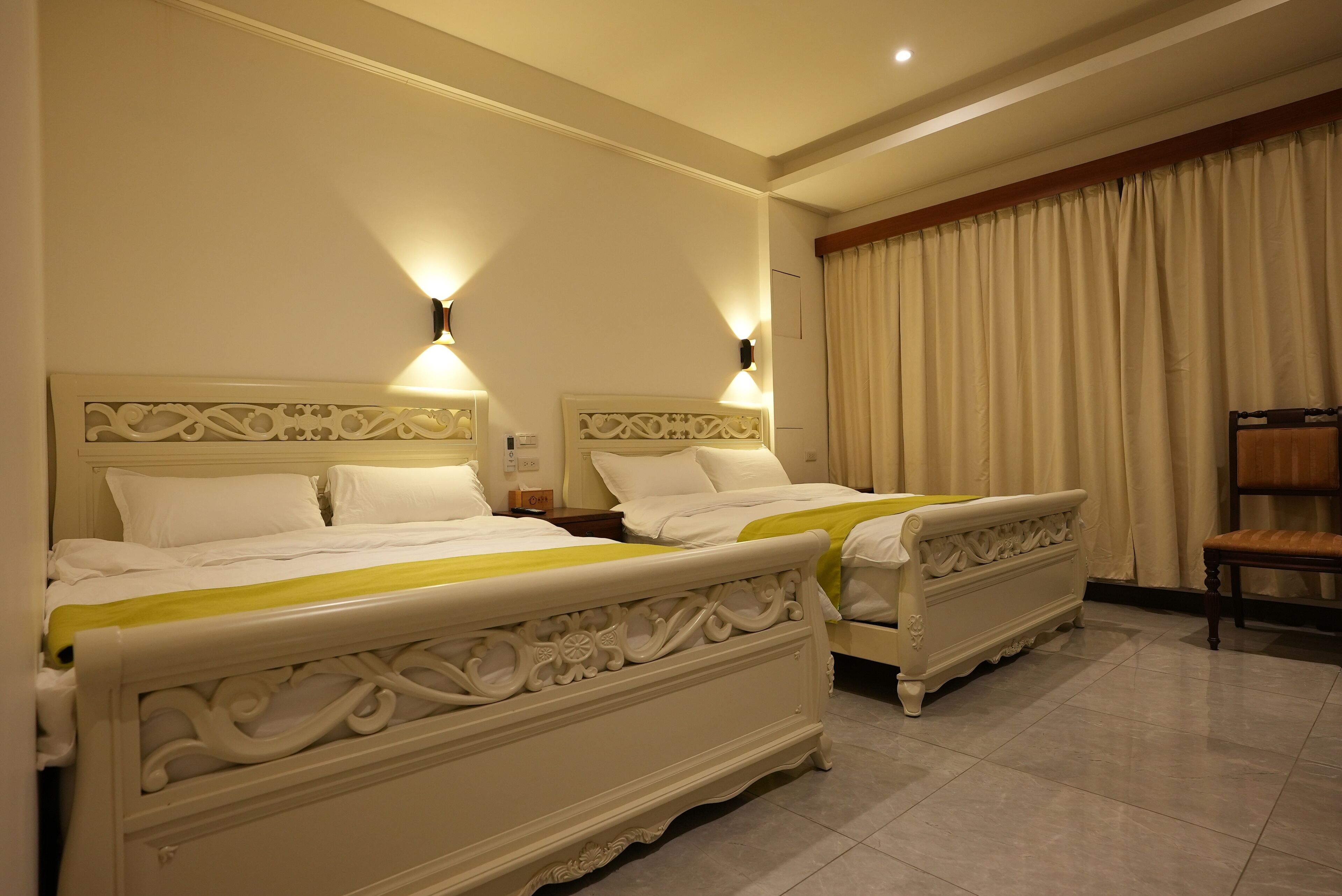 A hotel room with two beds, each with a decorative headboard and bedside lamps.