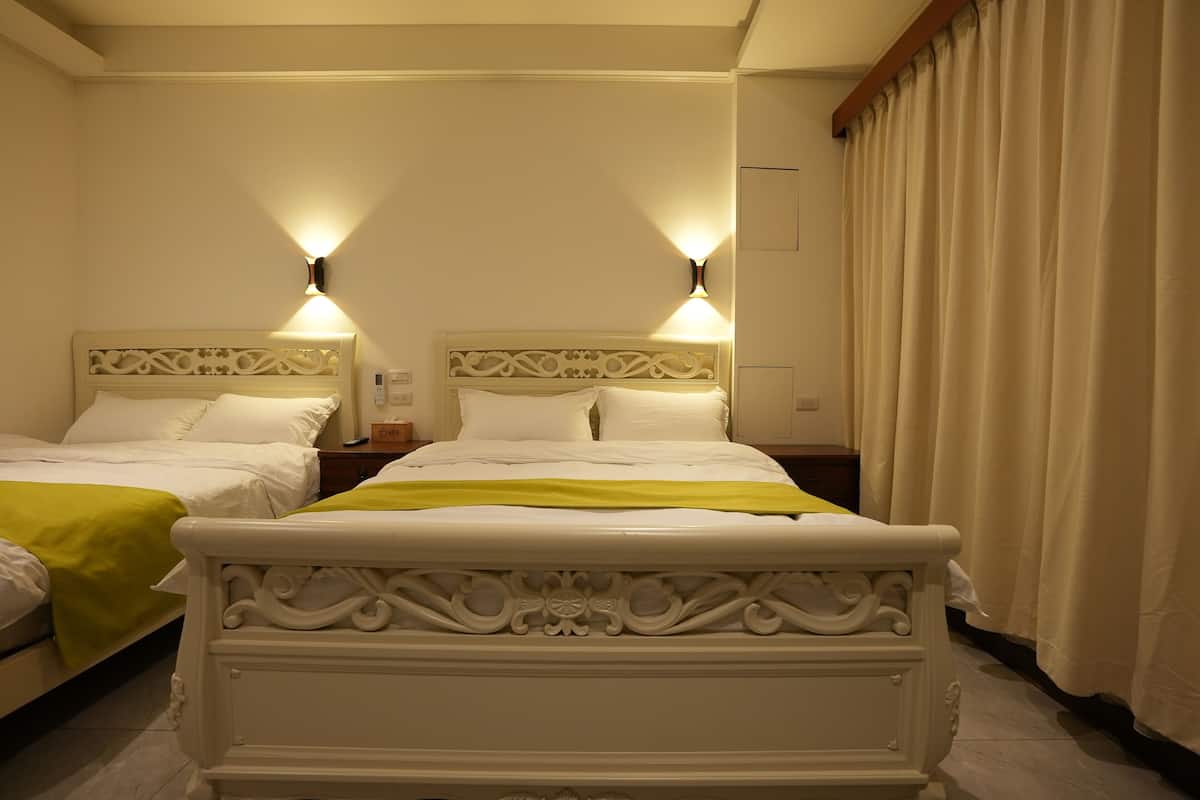 Quarto de hotel com duas camas, cada uma com cabeceira, mesas de cabeceira e luminárias.