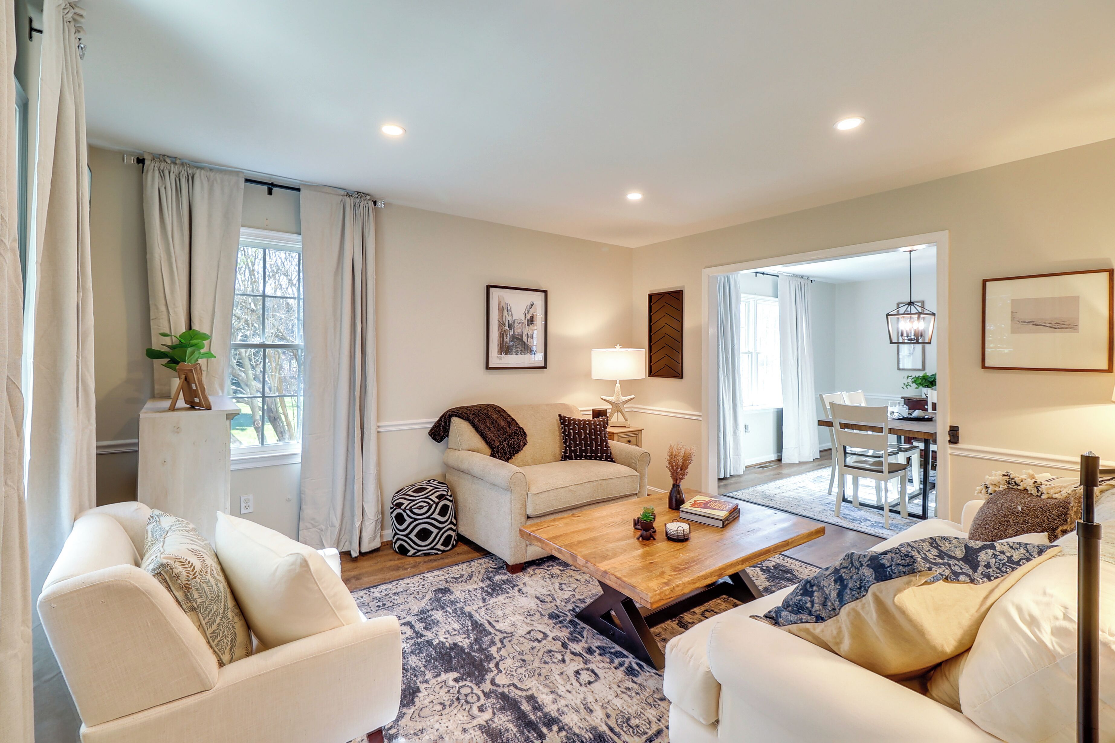 A living room with a sofa, armchairs, a coffee table, and a dining area in the background.