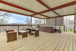 A covered outdoor deck with wicker furniture and a hot tub.