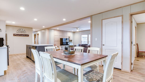 A spacious dining area with a wooden table and white chairs, a kitchen in the background, and a door leading to another room. - Hudson Oaks Country Creekside Home: Hot Tub & Deck (Weatherford)