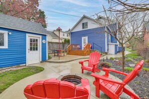 Un jardin avec un foyer, des fauteuils Adirondack rouges et une terrasse en bois.