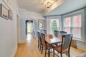 A dining area with a wooden table and chairs, a chandelier, and a view through large windows. - Ludington Home w/ 6 Bicycles < 1 Mi to Beach! (Ludington)