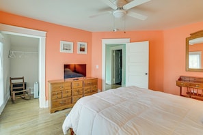 A bedroom with a bed, dresser, ceiling fan, and a door leading to another room.