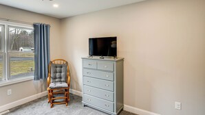 A room with a ceiling fan, a wooden chair, a grey dresser with a flat-screen TV, and a window with curtains. - Catskills Winter Getaway w/ Game Room (Greenville)