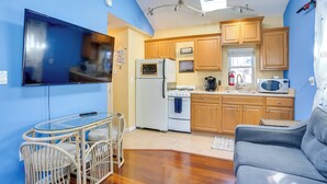 A compact kitchen with wooden cabinets, a refrigerator, stove, microwave, and a dining area with a glass table and chairs. - Greenwood Lake Cottage w/ Shared Dock & Hot Tub! (West Milford)