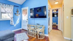 A room with a blue wall, a wooden dining table with chairs, a grey sofa, and a TV mounted on the wall. - Greenwood Lake Cottage w/ Shared Dock & Hot Tub! (West Milford)