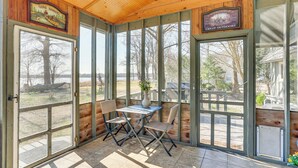A covered patio with a table and chairs, wooden walls, and large windows. - Boat Dock on Reelfoot Lake: Tiptonville Retreat (Tiptonville)