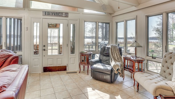 A spacious living room with a large window, a leather sofa, a tufted armchair, and a wooden side table. - Boat Dock on Reelfoot Lake: Tiptonville Retreat (Tiptonville)