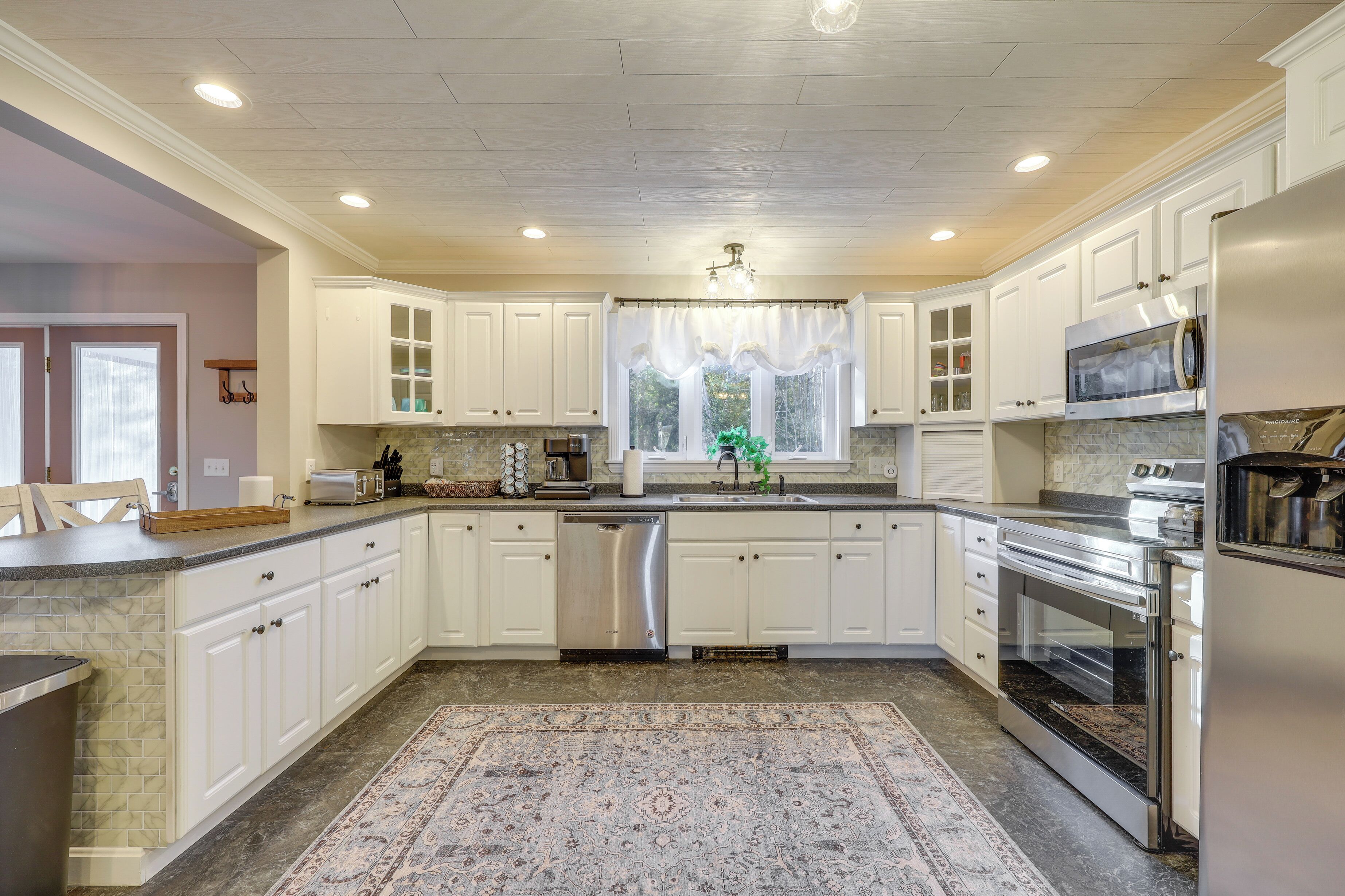 A modern kitchen with white cabinets, stainless steel appliances, and a patterned rug.