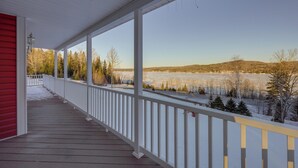 A covered porch with white railings, a red wall on one side, and a view of a frozen landscape with trees and hills in the distance.
