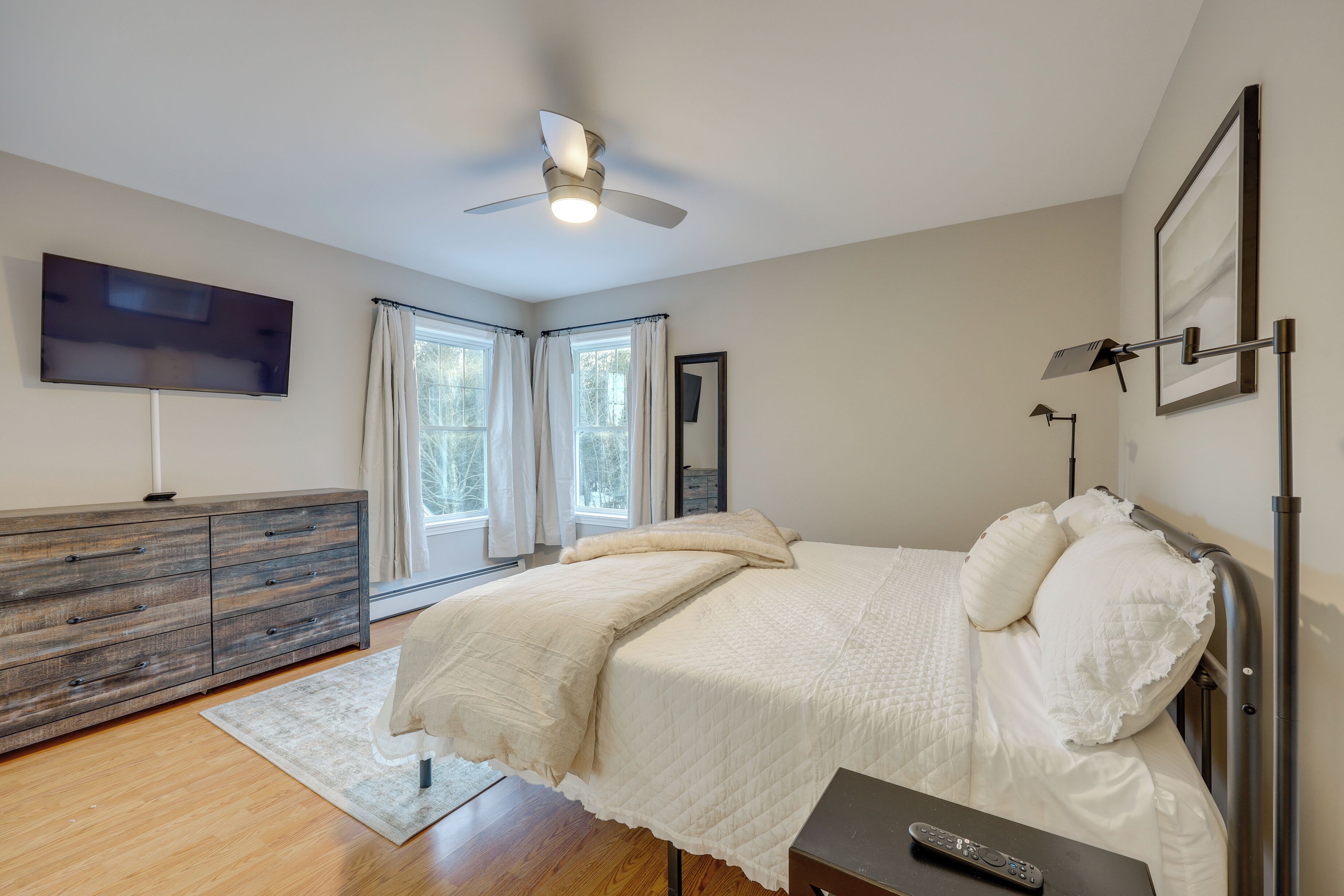 A bedroom with a bed, a dresser, a TV, and a ceiling fan.
