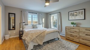 A bedroom with a bed, a ceiling fan, a dresser, and a window with curtains.