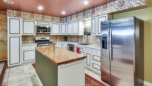 A kitchen with white cabinets, a stainless steel refrigerator, a microwave, and a wooden island. - Smethport Vacation Rental w/ Fireplace & Lake View (Smethport)