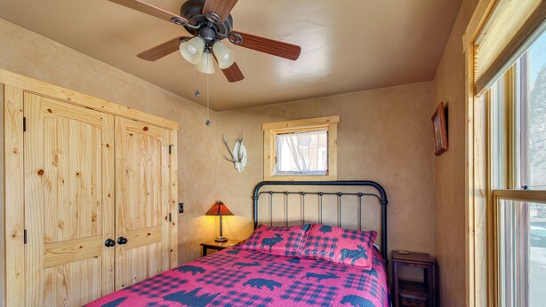 A bedroom with a bed, wooden wardrobe, ceiling fan, window, and a wall-mounted deer skull. - Cozy Ouray Hideaway: Mountain Views, Steps to Main (Ouray)