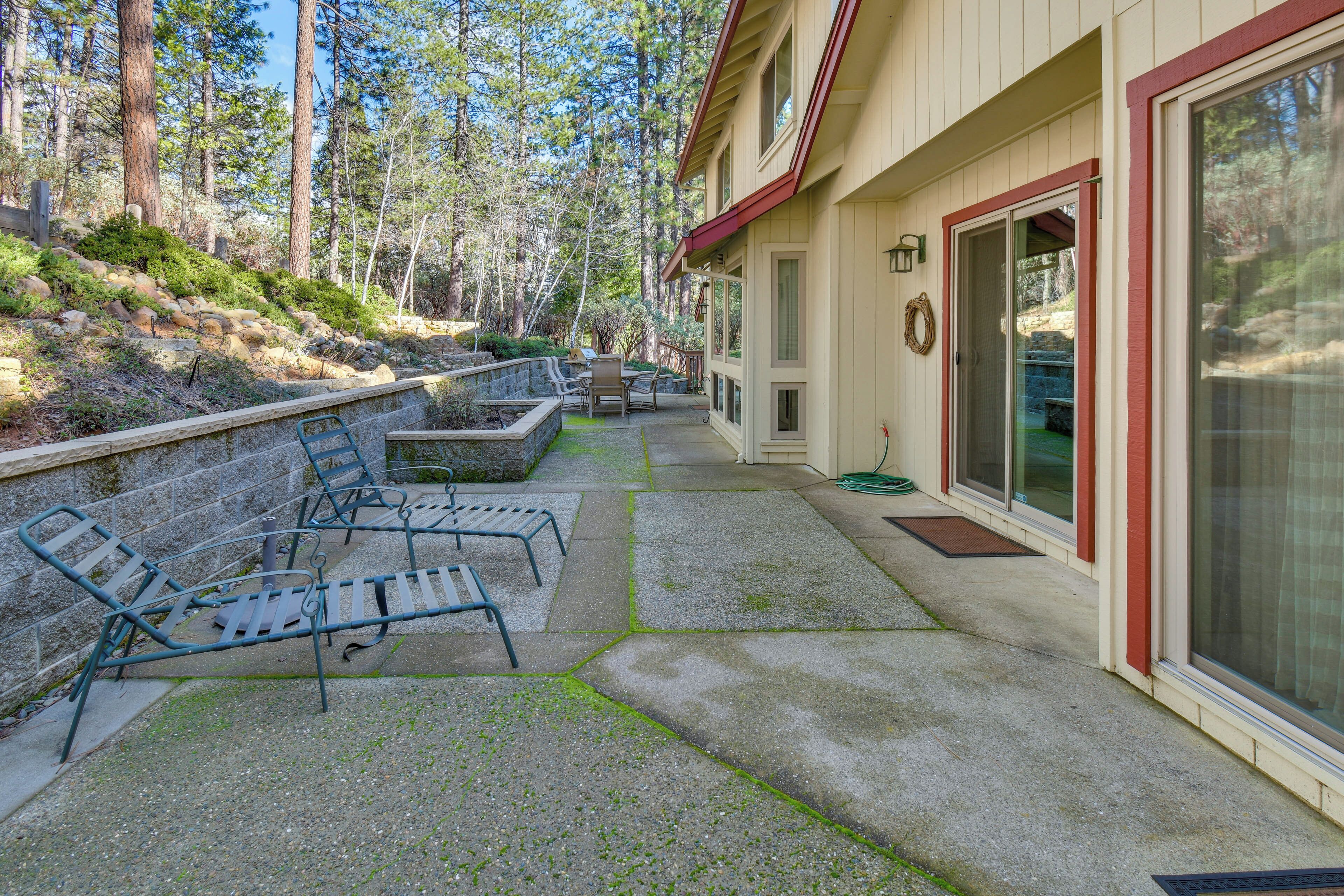 A covered outdoor patio with seating, a stone retaining wall, and a building with a red trim and large sliding glass doors.