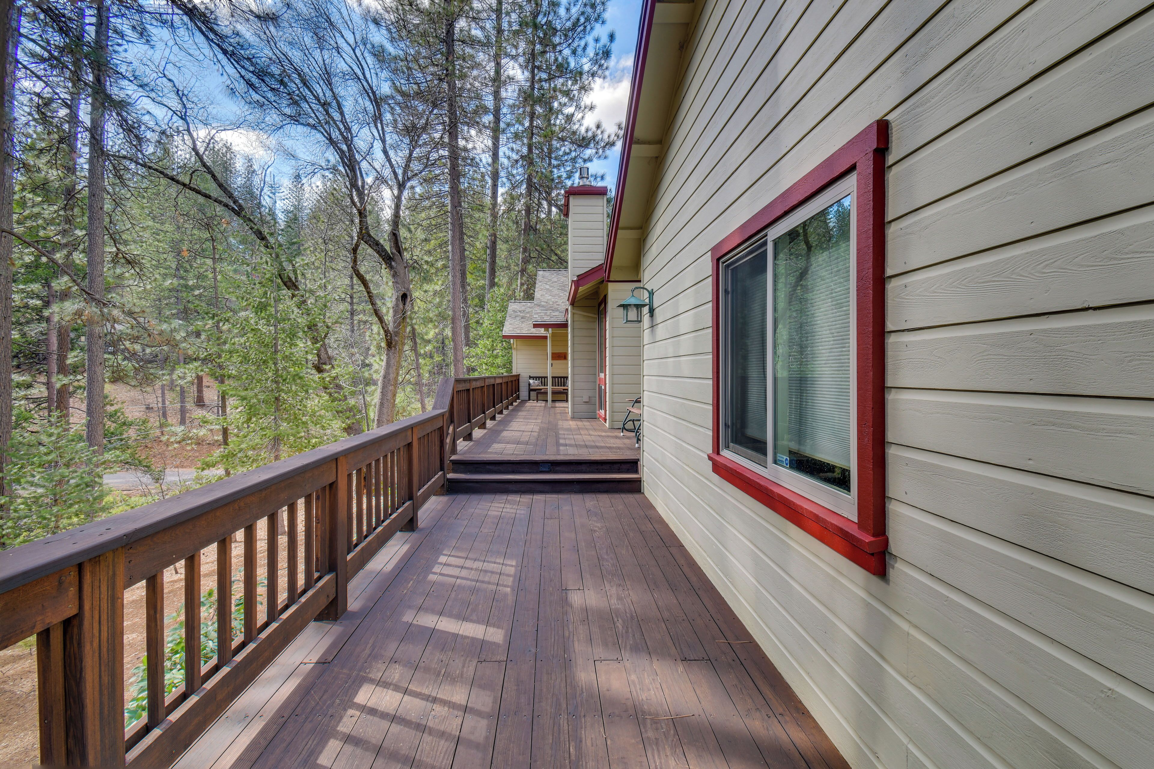 A wooden deck with a railing, leading to a house with a large window and a chimney.