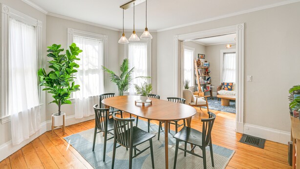 A dining area with a wooden table and chairs, surrounded by potted plants and large windows with sheer curtains. - Bright & Pet-friendly Home: 2 Mi to Harvard Square (Watertown)