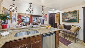 A kitchen with granite countertops, a stainless steel sink, and a dishwasher. There is a dining area with a bench and a painting on the wall. - Vail Condo w/ Pool, Hot Tub & Free Bus Access (Vail)