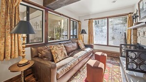 A cozy living room with a leather sofa, patterned curtains, and a large window with a view of a snowy landscape. - Vail Condo w/ Pool, Hot Tub & Free Bus Access (Vail)