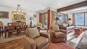 A spacious living room with a wooden dining table, leather sofas, and a large window with a view of trees. - Vail Condo w/ Pool, Hot Tub & Free Bus Access (Vail)