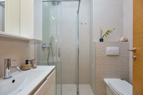 Un baño moderno con cabina de ducha de vidrio, un lavamanos blanco y un inodoro.