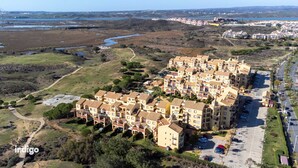A residential area with a row of multi-story buildings, a parking lot, and a river in the background. - GUA001 (Ayamonte)