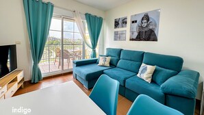 A modern living room with a teal sofa, a TV, and a dining table. - GUA001 (Ayamonte)