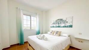 A bedroom with a bed, curtains, a window, and a wall-mounted painting. - GUA001 (Ayamonte)