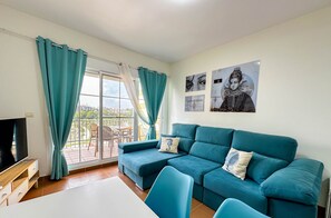 Un salon moderne avec un canapé de couleur turquoise, un téléviseur et une table à manger.