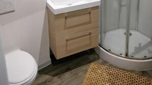 A modern bathroom with a white sink, wooden vanity, and a glass-enclosed shower. - Logement 3 (Les Epesses)