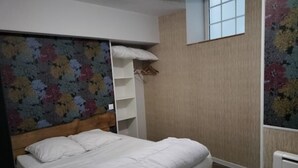 A bedroom with a wooden bed, white bedding, a floral-patterned headboard, a white wardrobe, and a window with a view of trees. - Logement 3 (Les Epesses)