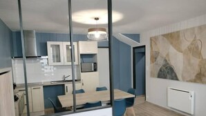 A modern kitchen with white cabinets, a microwave, and a dining area with a table and chairs. - Logement 3 (Les Epesses)