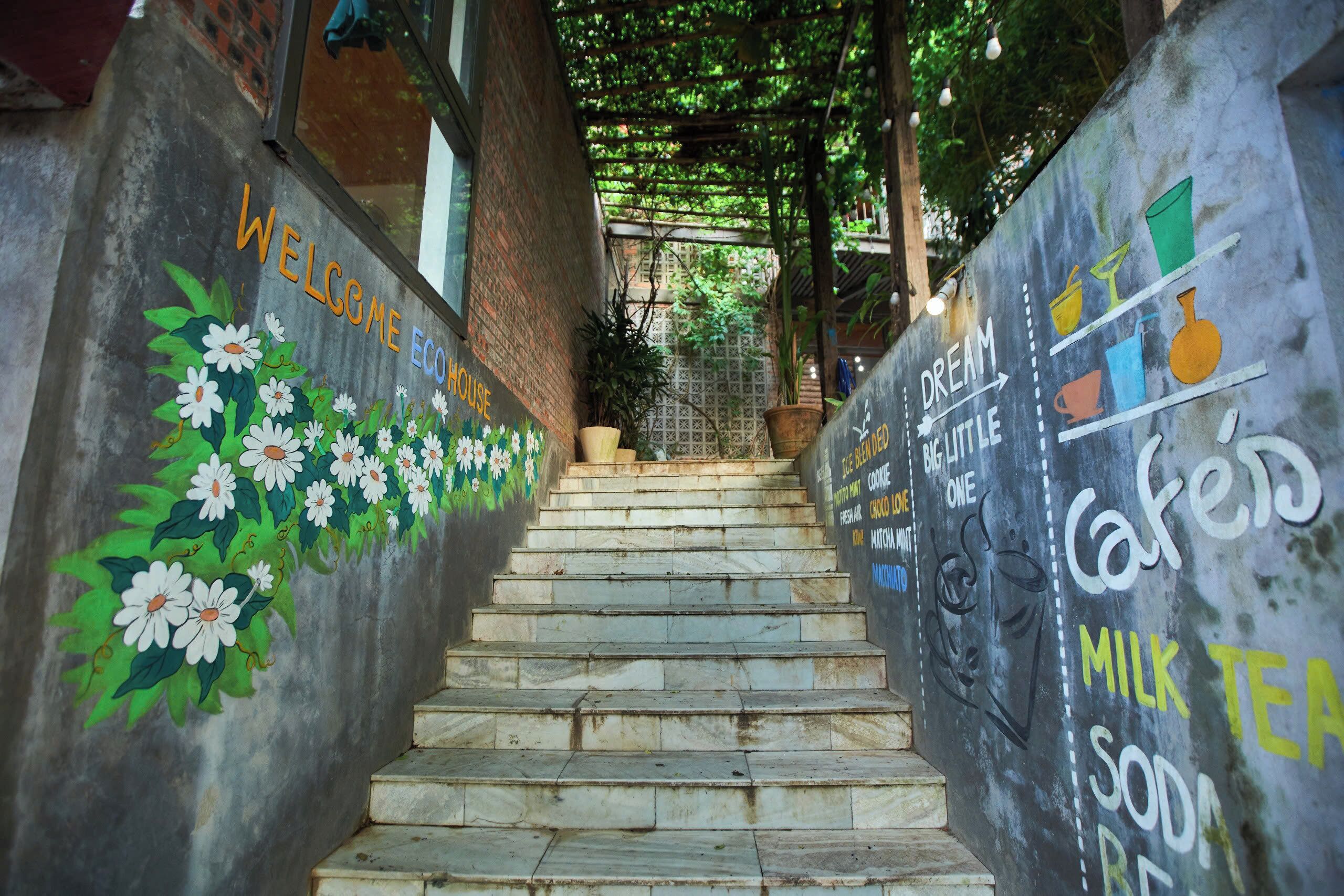 A staircase with a mural on the walls, leading to a covered area with plants.