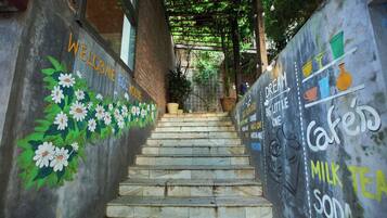 A staircase with a mural on the walls, leading to a covered area with plants.
