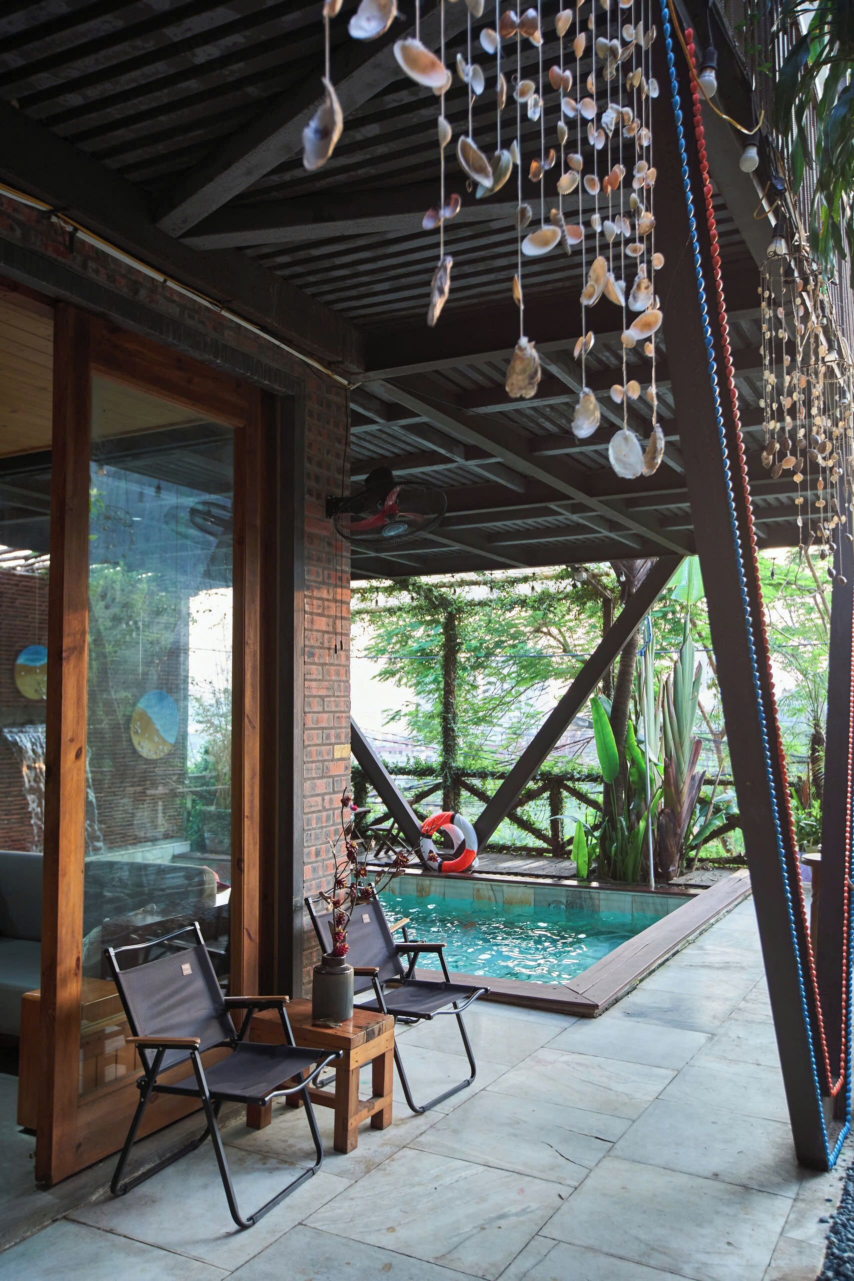 Un espacio al aire libre techado con piscina, sillas de descanso y conchas colgantes.