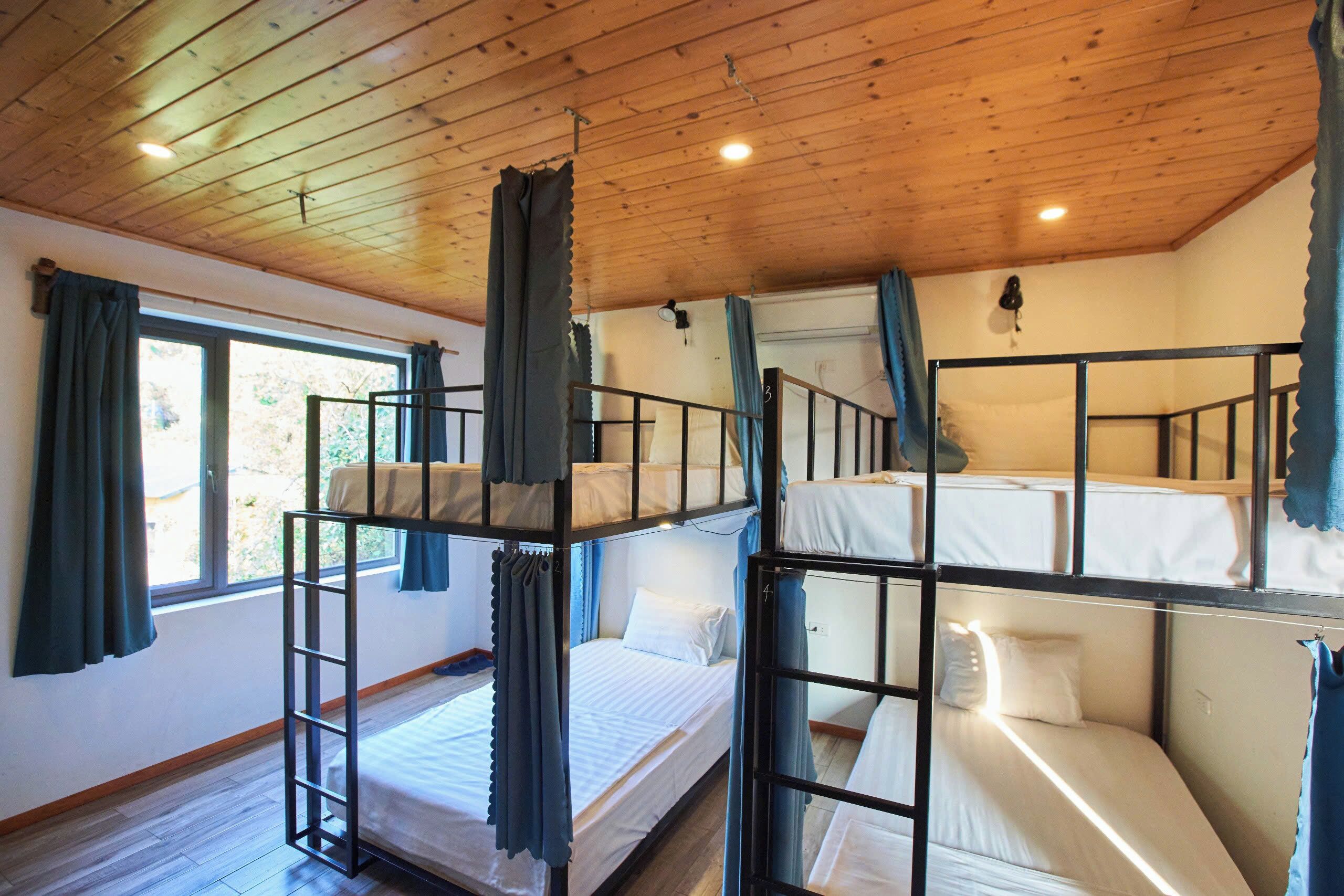 Una habitación con literas, techo de madera y una ventana con cortinas.