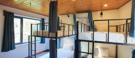 Una habitación con literas, techo de madera y una ventana con cortinas.