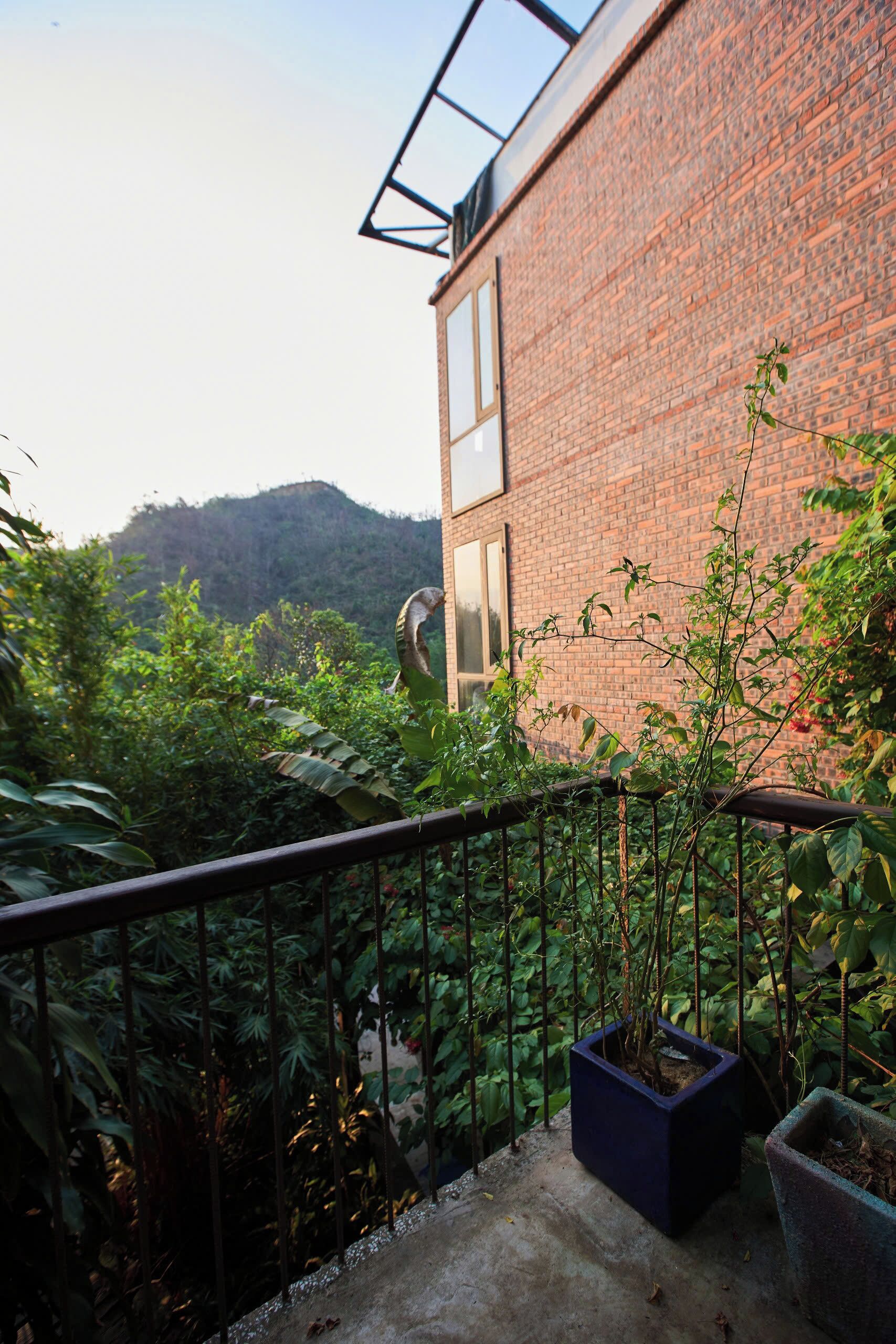 Ein Balkon mit Blick auf ein Backsteingebäude, üppiges Grün und eine ferne Hügellandschaft.