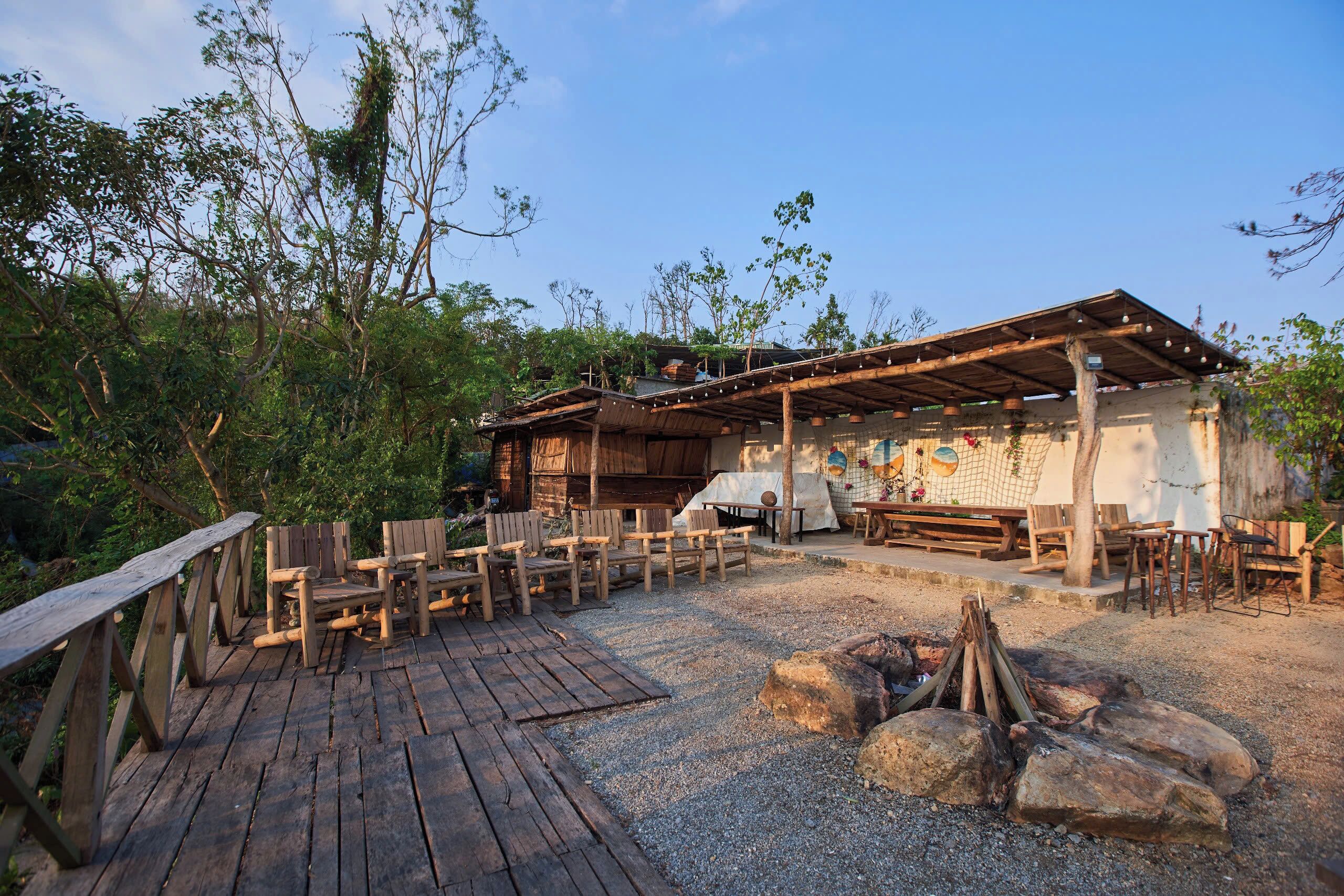 A rustic outdoor seating area with wooden benches and a fire pit, surrounded by trees.