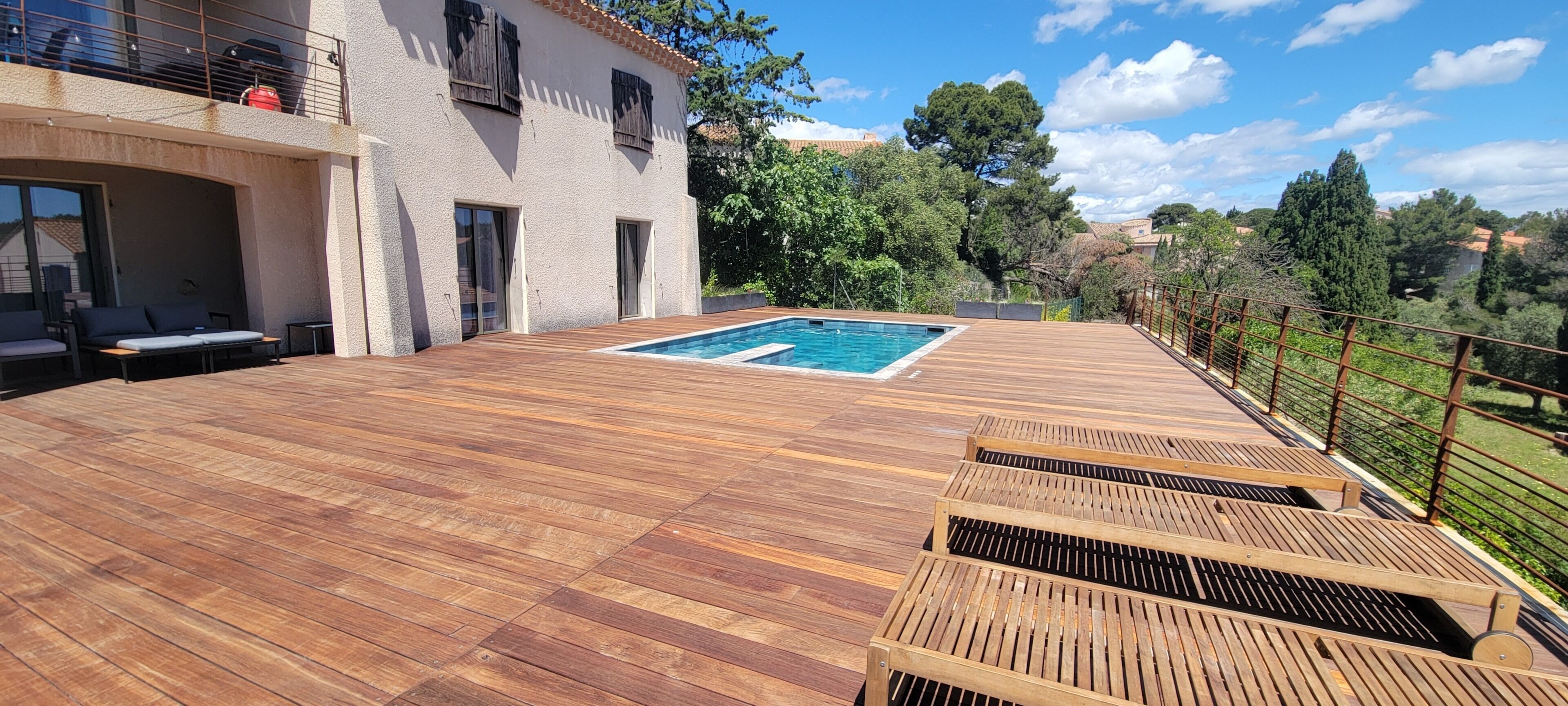 A wooden deck with a pool, outdoor seating, and a view of the surrounding landscape.