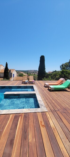 Una terraza de madera con piscina, sillas de descanso y vistas del paisaje circundante.