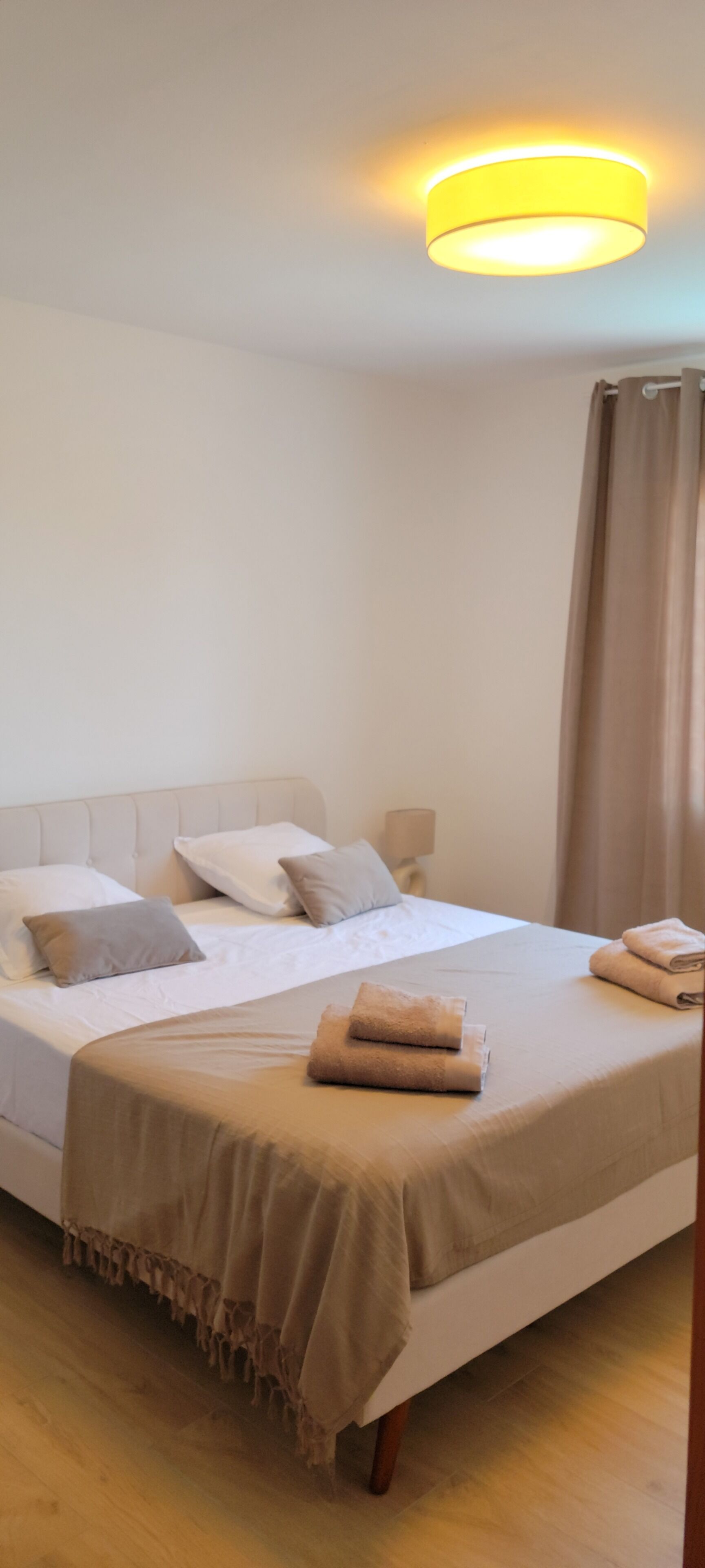 Una camera da letto con un letto, cuscini, un comodino, una lampada e una tenda.