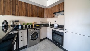 A modern kitchen with wooden cabinets, a washing machine, an oven, and a coffee maker.