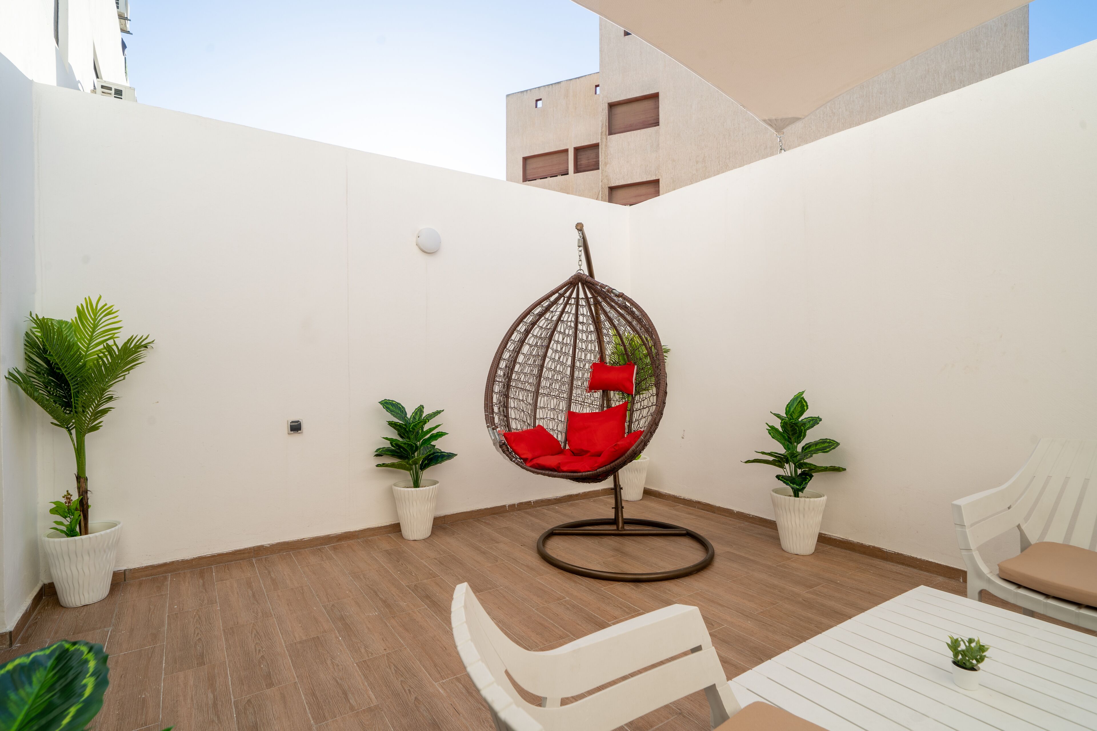 A modern outdoor seating area with a hanging chair, white lounge chairs, and potted plants.