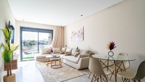 A modern living room with a sofa, coffee table, and chairs, a glass dining table, and a large window with a view.